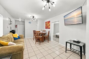 A modern living room with a sofa, dining table, chairs, and a TV. - Cute cottage across from the Gulf (Gulf Shores)