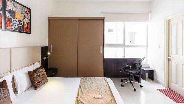 Une chambre d’hôtel avec un lit, un bureau, une chaise, une armoire et un tableau au mur.