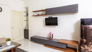 Un salon moderne doté d’un téléviseur à écran plat fixé au mur, d’un meuble en bois intégré en dessous et d’un réfrigérateur orné de motifs floraux.
