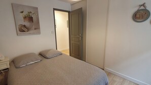 Et soveværelse med seng, puder, et natbord, en lampe, en dør og et billede hængt på væggen.