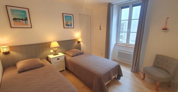 A hotel room with two beds, a nightstand, a chair, and a window with curtains.