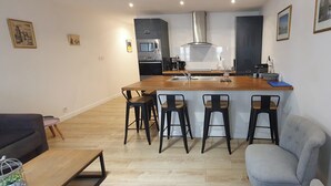 Et moderne køkken med en central ø, barstole, et spiseområde med en sofa og et lille bord.