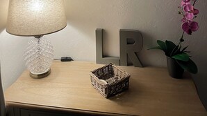 Et værelse med et træbord, en lampe, en dekorativ væg med hjerteformede dekorationer og en orkidé i en potte.