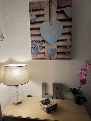 Une pièce avec une table en bois, une lampe, un mur décoratif orné de motifs en forme de cœur et une plante orchidée en pot.