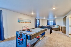Une table de billard, une table de baby-foot et un canapé dans un salon, avec un tableau accroché au mur.