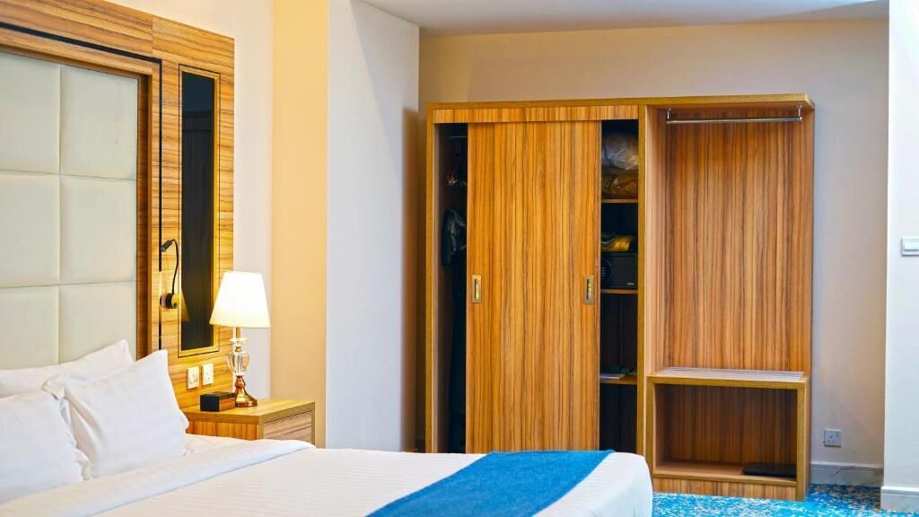 Une chambre d’hôtel comprenant un lit, une table de chevet, une lampe, une armoire en bois et une étagère.