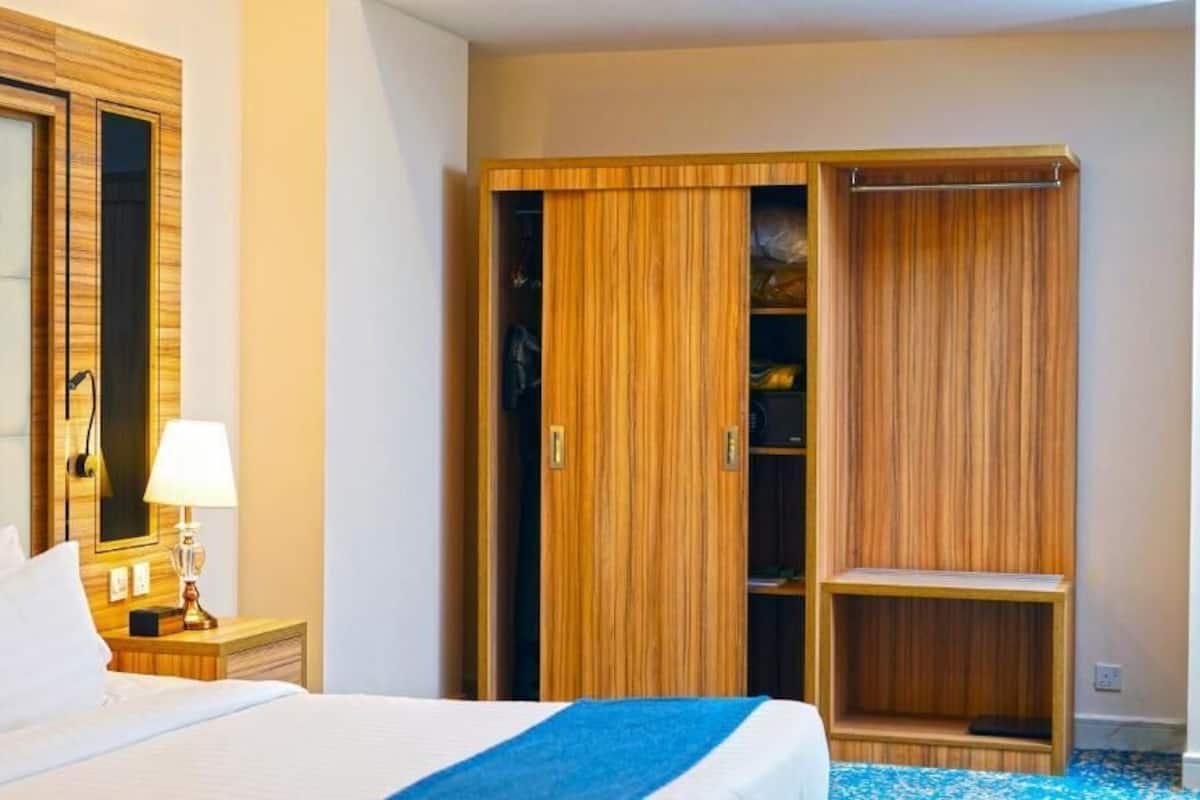 Une chambre d’hôtel comprenant un lit, une table de chevet, une lampe, une armoire en bois et une étagère.