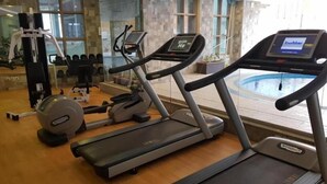 Une salle de sport équipée de tapis de course, d’appareils de musculation et d’une piscine visible à travers les fenêtres.