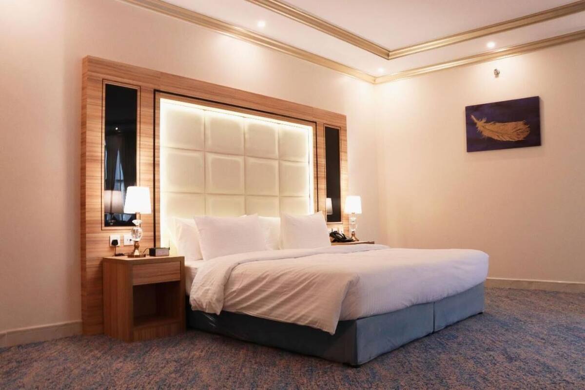 Une chambre d’hôtel avec un grand lit, une tête de lit en bois, deux tables de chevet et une œuvre d’art accrochée au mur.