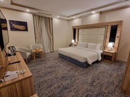 A hotel room with a large bed, two bedside tables, a desk with a telephone, a chair, and a carpeted floor.