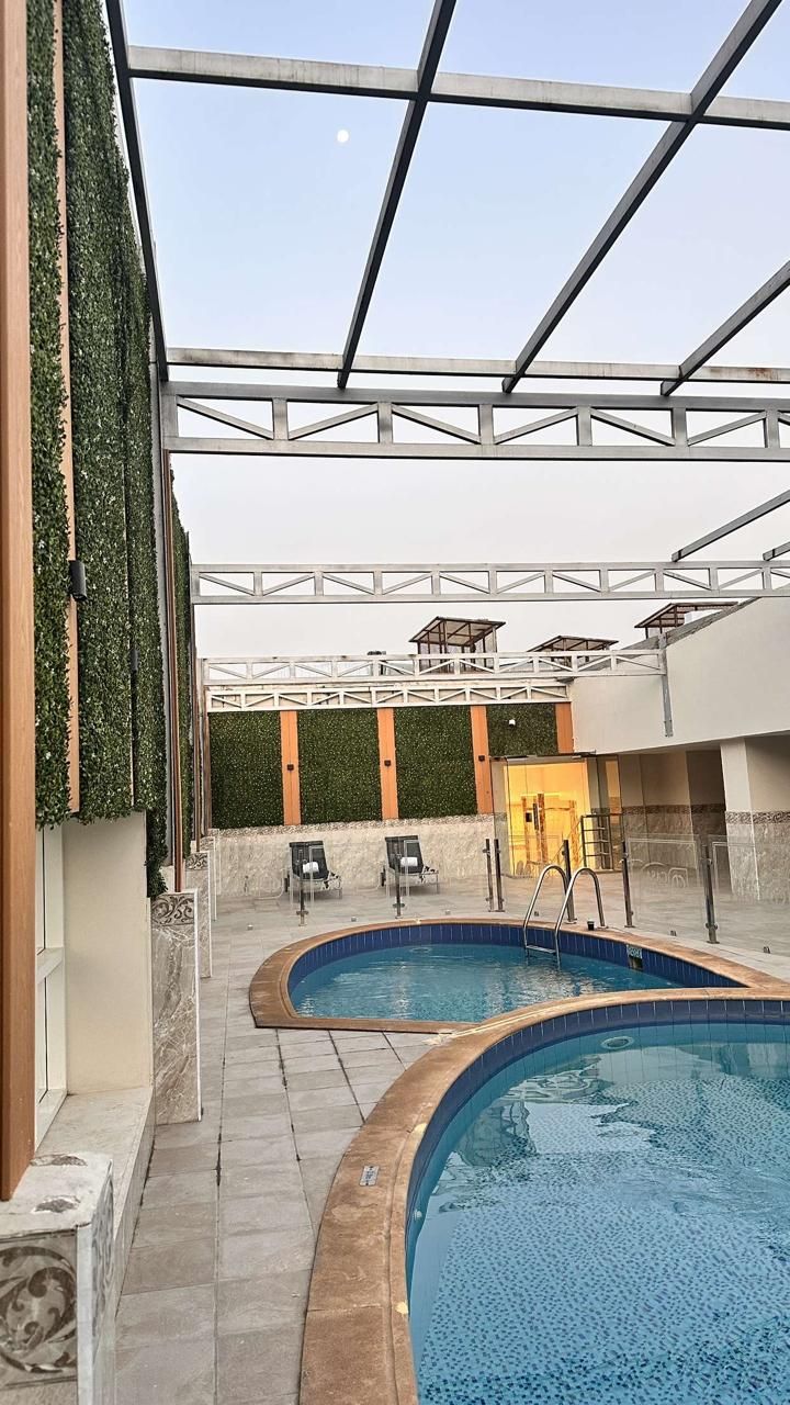 Una piscina interior con techo de vidrio, rodeada de sillones de descanso y una pared con plantas.