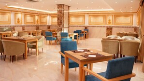 Un vaste espace de restauration d’hôtel, doté de nombreuses tables et chaises, et présentant un design épuré et moderne, agrémenté de touches de marbre et d’un éclairage chaleureux.