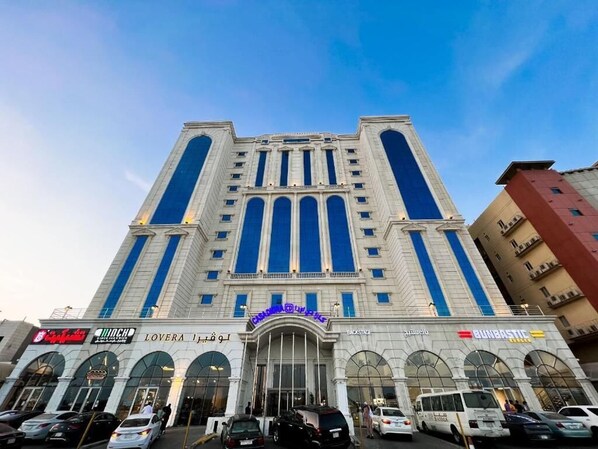 A large, multi-story building with a central entrance featuring arched windows and a blue sign above. - Casa Diora Hotel Al Naseem (Jeddah)