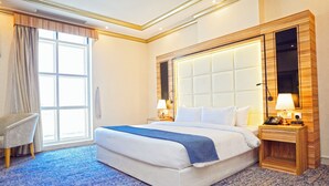 Une chambre d’hôtel avec un grand lit, une chaise, un bureau avec un téléphone et un miroir.