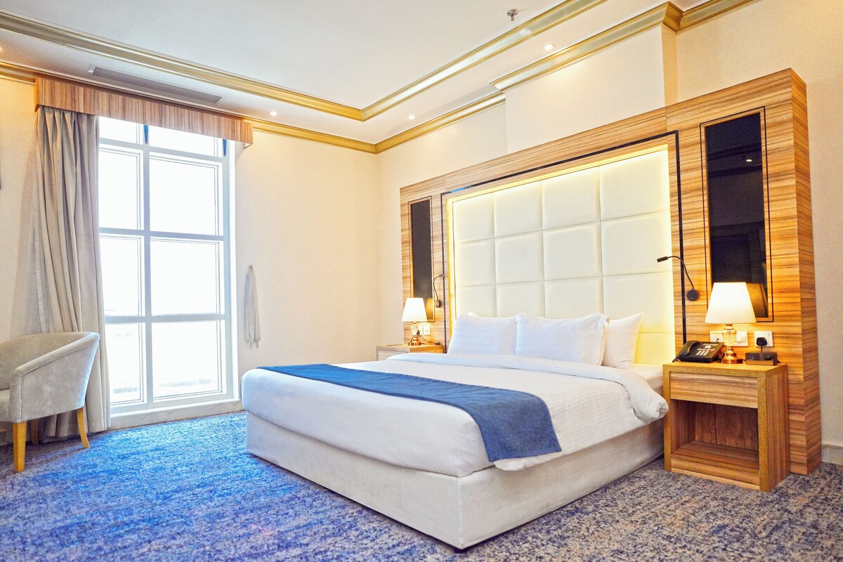 A hotel room with a large bed, a chair, a desk with a phone, and a mirror.
