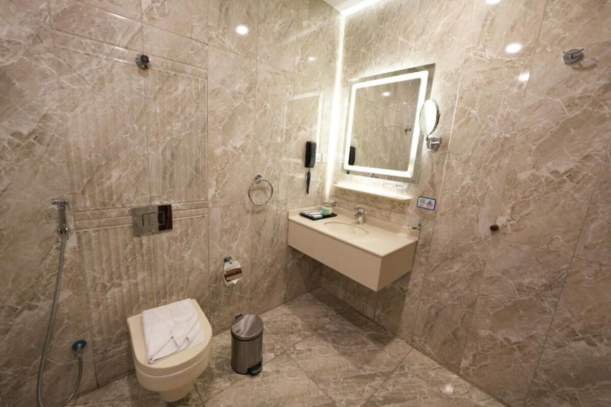 Une salle de bain avec un sol en marbre, des toilettes, un lavabo avec un miroir et une douchette à main.