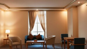 Une chambre d’hôtel avec un canapé, deux fauteuils, une petite table et une fenêtre avec des rideaux.
