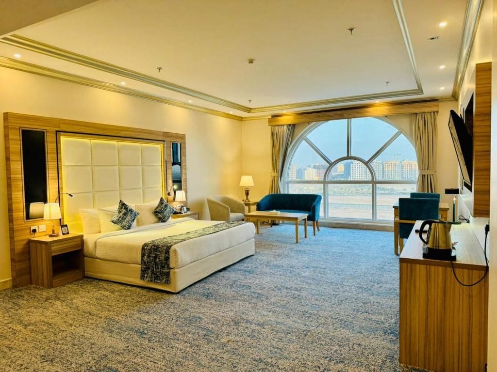 A hotel room with a large bed, a desk, a chair, and a view of the city.