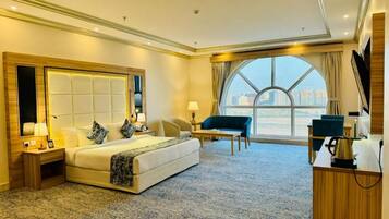 A hotel room with a large bed, a desk, a chair, and a view of the city.