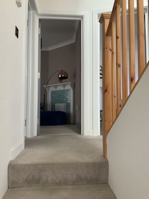 A carpeted staircase leading to a room with a blue tiled fireplace, a lamp, and a bed.