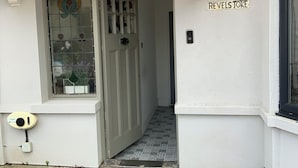 Un bâtiment blanc avec un toit à pignon en bois, une porte en verre ornée de motifs décoratifs et une enseigne indiquant « REVELS TOKE ».