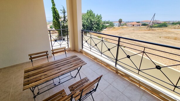 Een balkon met houten bankjes en een metalen hekwerk met uitzicht op een droog veld en verre gebouwen.