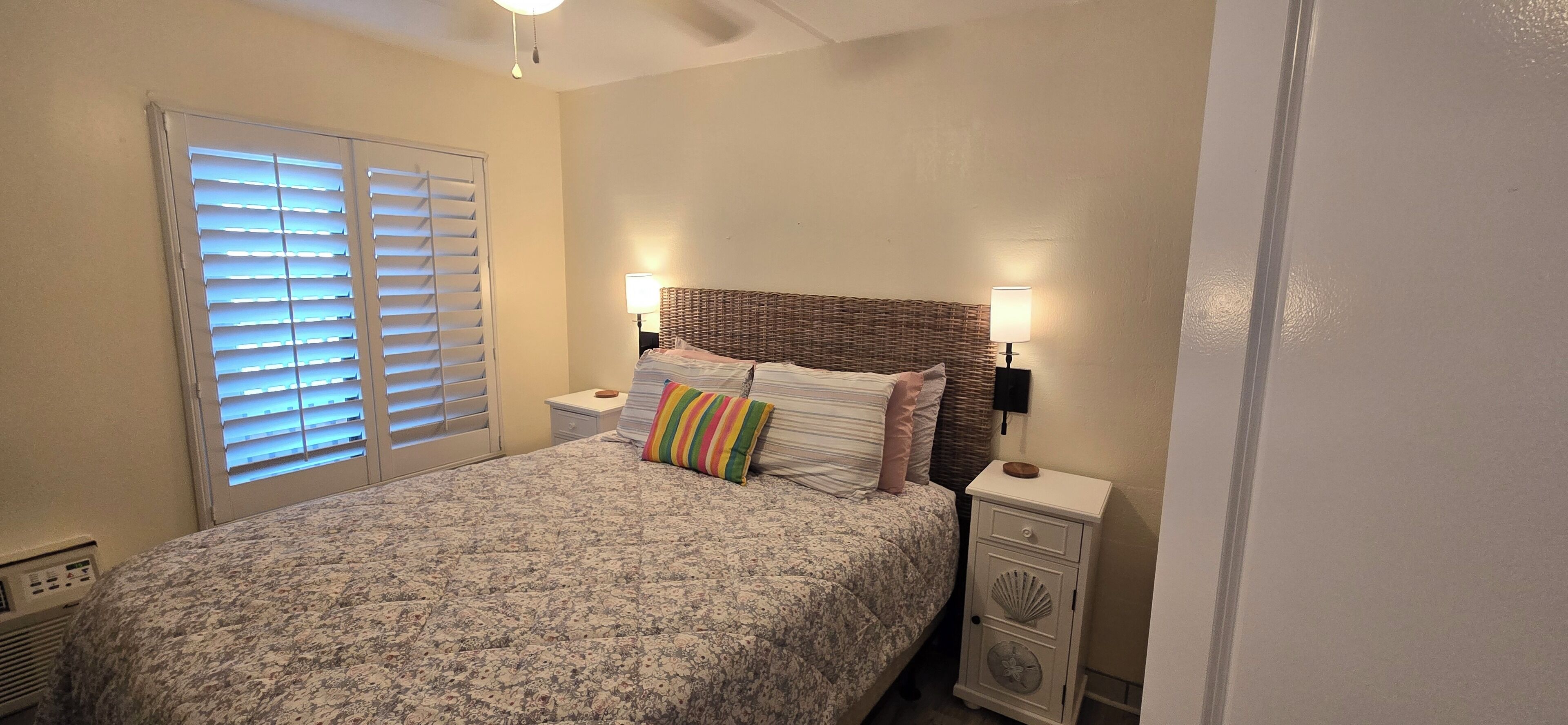 Une chambre à coucher avec un lit, des tables de chevet, une lampe et une fenêtre avec des stores.