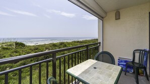 Ein Balkon mit Tisch und Stühlen mit Blick auf einen Strand, in der Ferne sind Personen zu sehen.