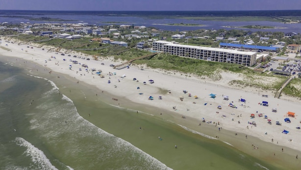 Ein Küstenhotel mit mehreren Gebäuden, einem Strand mit Sonnenschirmen und einem Steg.
