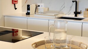A modern kitchen with a marble backsplash, a black faucet, and a woven tray with glasses. - Front Sea Apartment Albufeira (Albufeira)