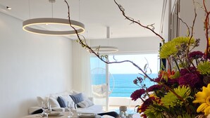 A dining area with a view of the sea, a white sofa, and a table set for four with glasses and plates. - Front Sea Apartment Albufeira (Albufeira)