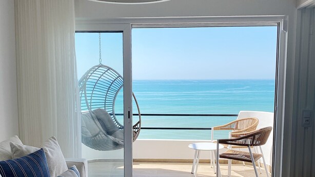 A modern living room with a sofa, a glass coffee table, and a view of the ocean through a sliding glass door. - Front Sea Apartment Albufeira (Albufeira)