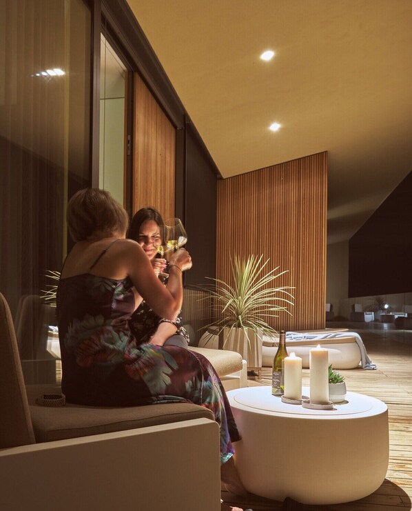 A modern indoor setting with two people seated on a sofa, a round table with candles, and a potted plant.