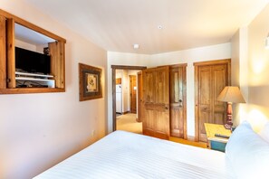 A bedroom with a bed, wooden wardrobe, a television, and a lamp.