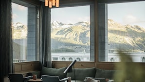 Ein Zimmer mit Blick auf Berge und eine Brücke. Stühle und Tische sind zum Sitzen aufgestellt.