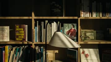 Una estantería con varios libros, una lámpara y un cartel sobre mujeres que transformaron la arquitectura.