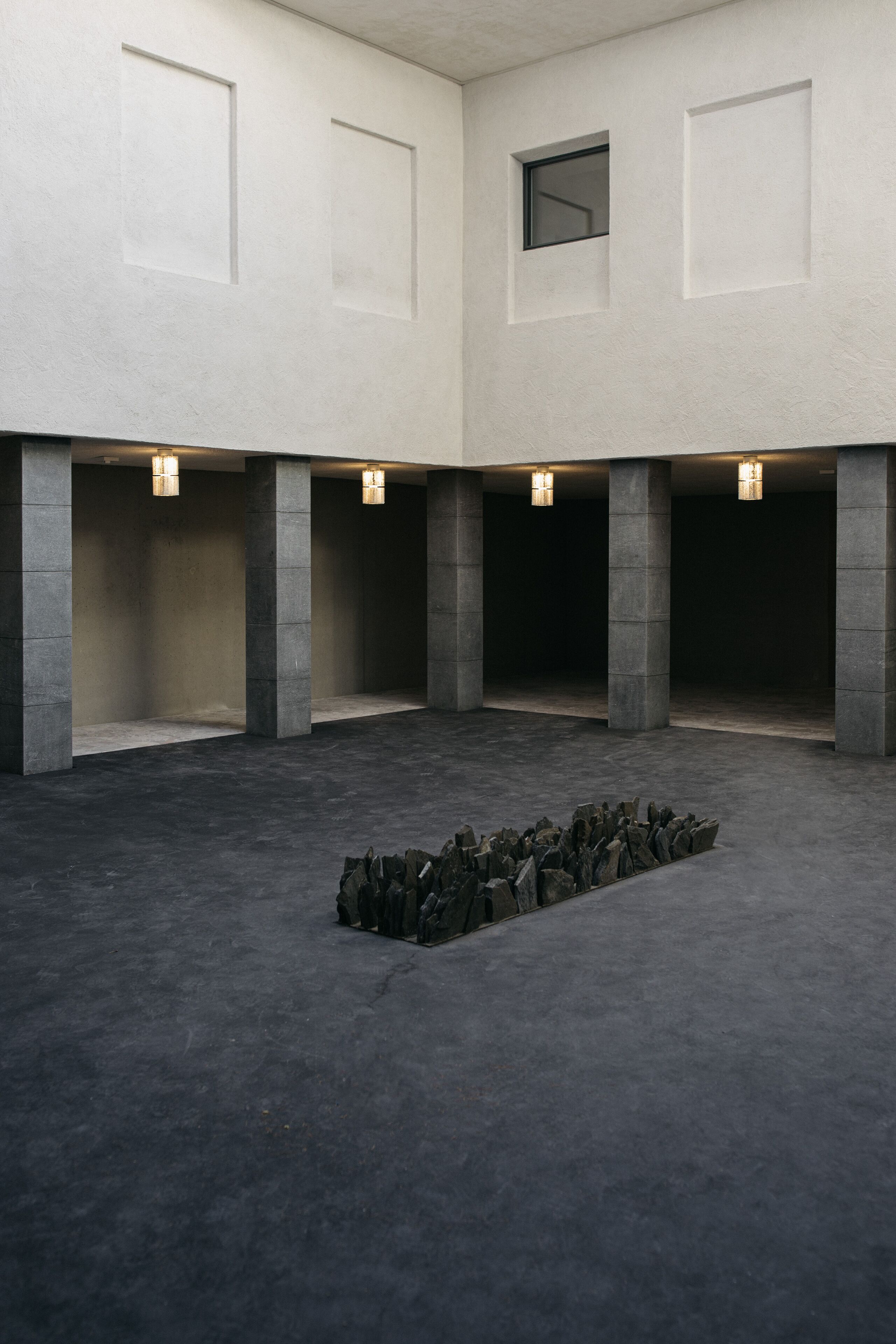 Um espaço amplo com uma disposição central de pedras, pilares de concreto e iluminação embutida.