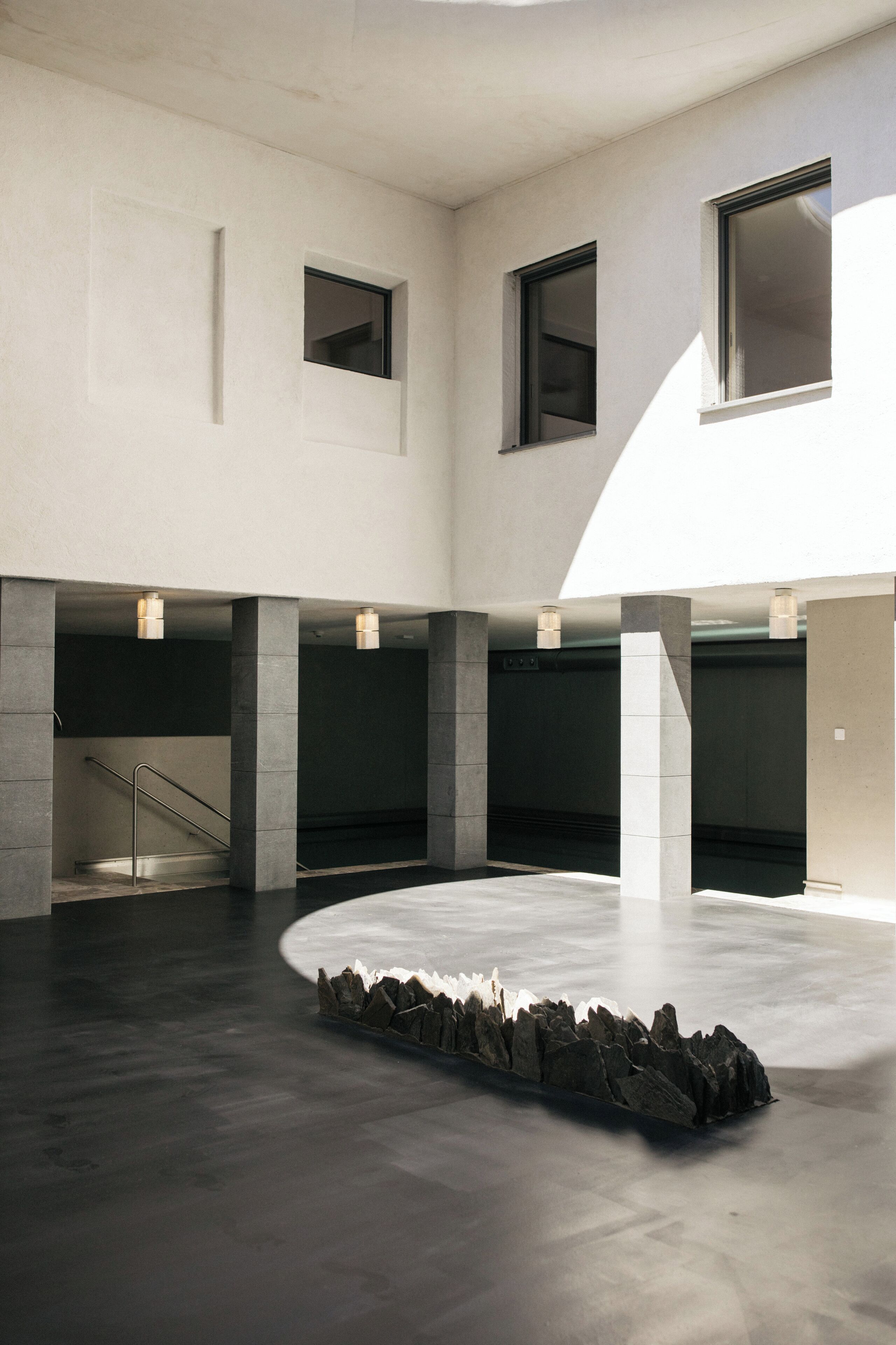 Un interior espacioso y moderno con un área central abierta, pilares de hormigón y una escalera.