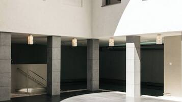 Un interior espacioso y moderno con un área central abierta, pilares de hormigón y una escalera.