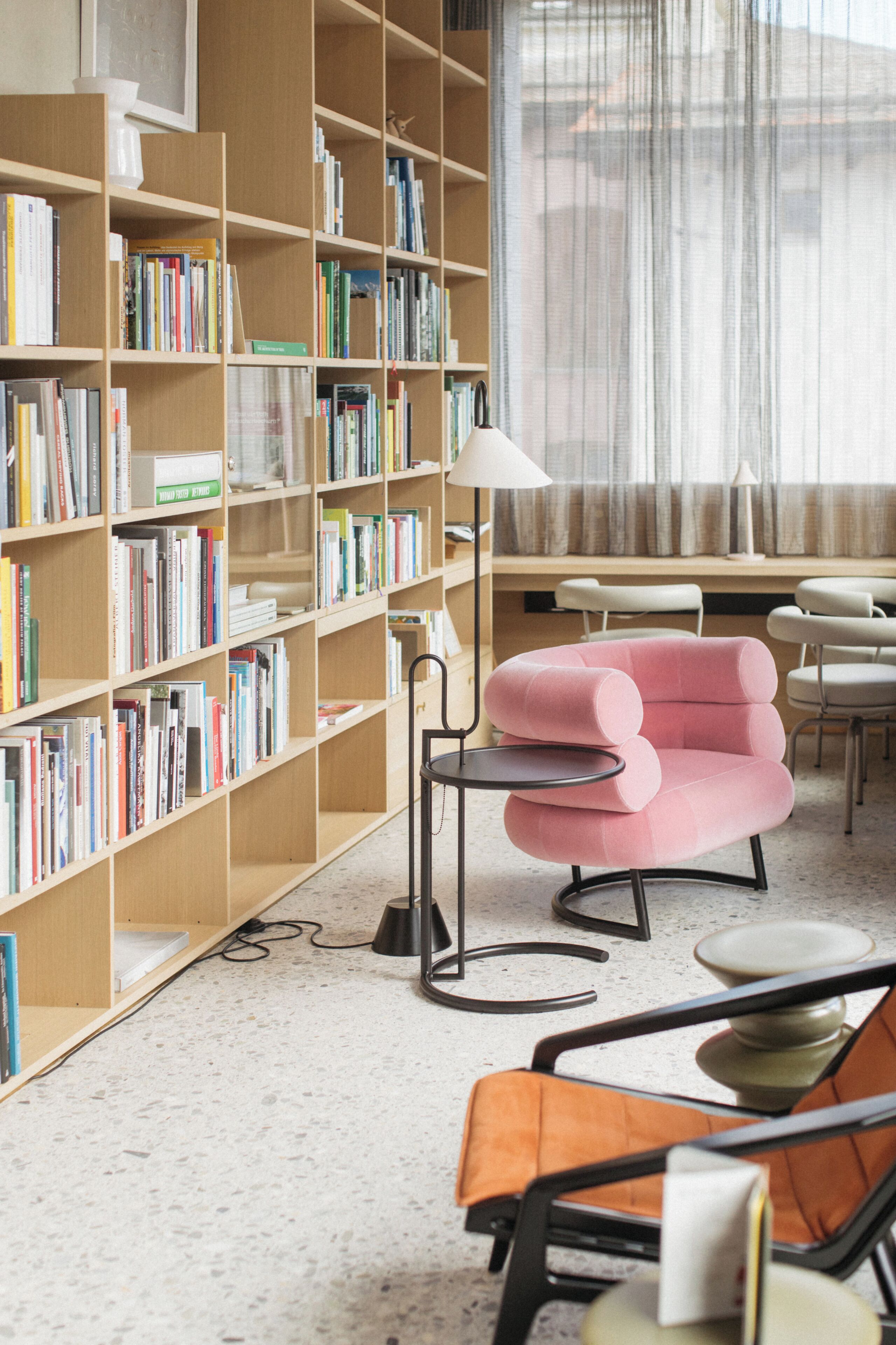 A library with bookshelves, a pink armchair, and a round table.