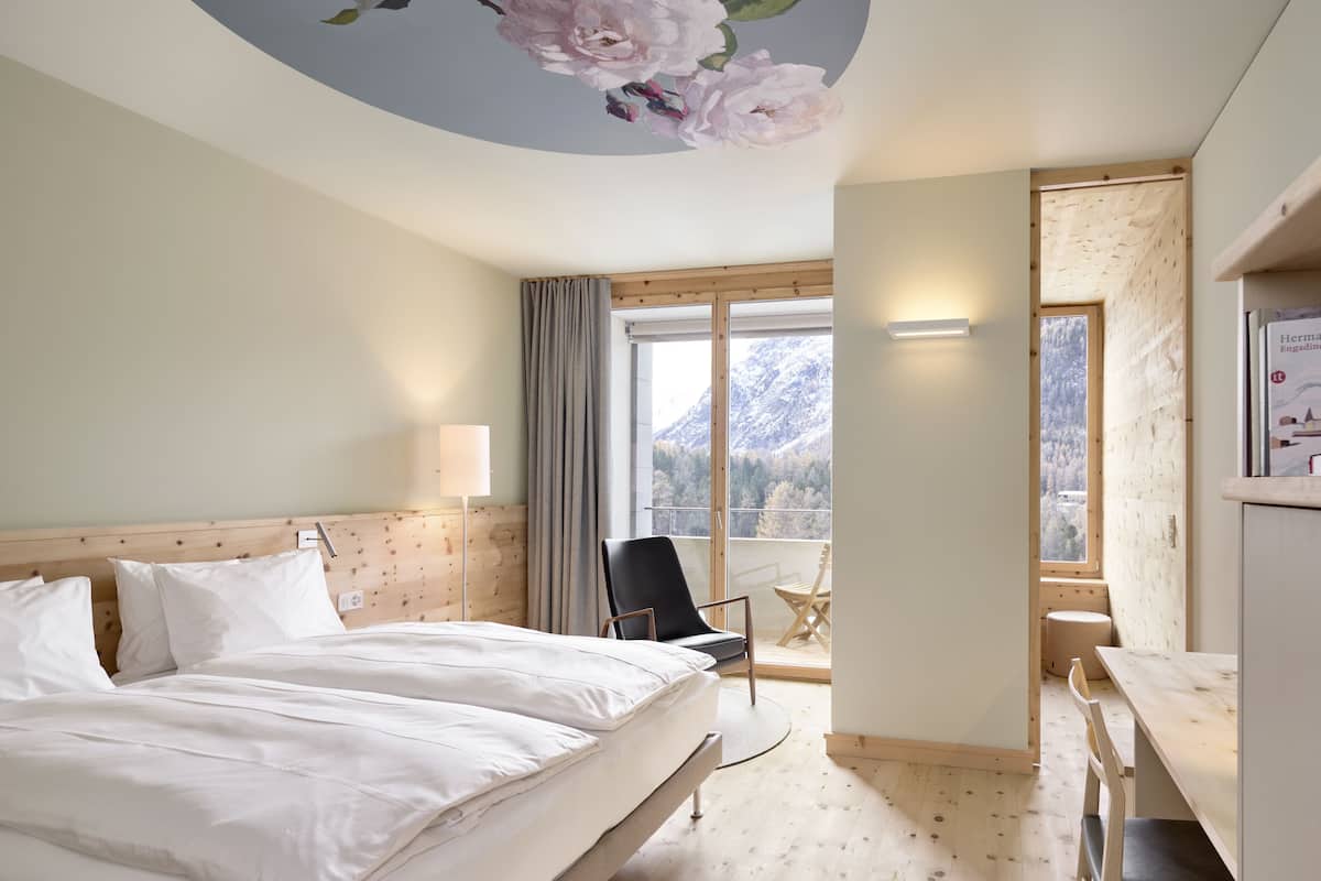 Une chambre d’hôtel avec un grand lit, un bureau, une chaise et un balcon offrant une vue sur la montagne.