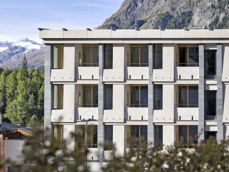 A modern building with multiple balconies and large windows, set against a mountainous backdrop.