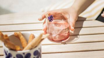 A hand holding a glass with a flower, a cup with breadsticks, and a wooden table.