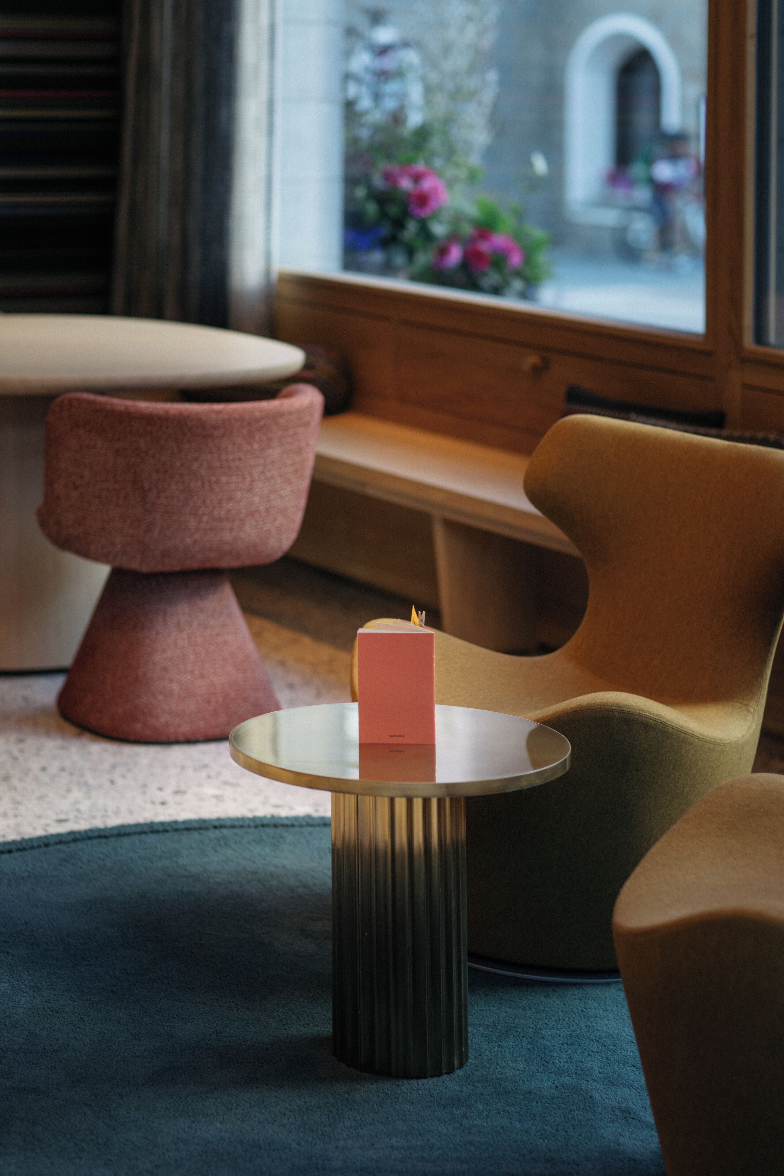 A modern living room with a round glass coffee table, a pink candle, and a view of a garden through a window.