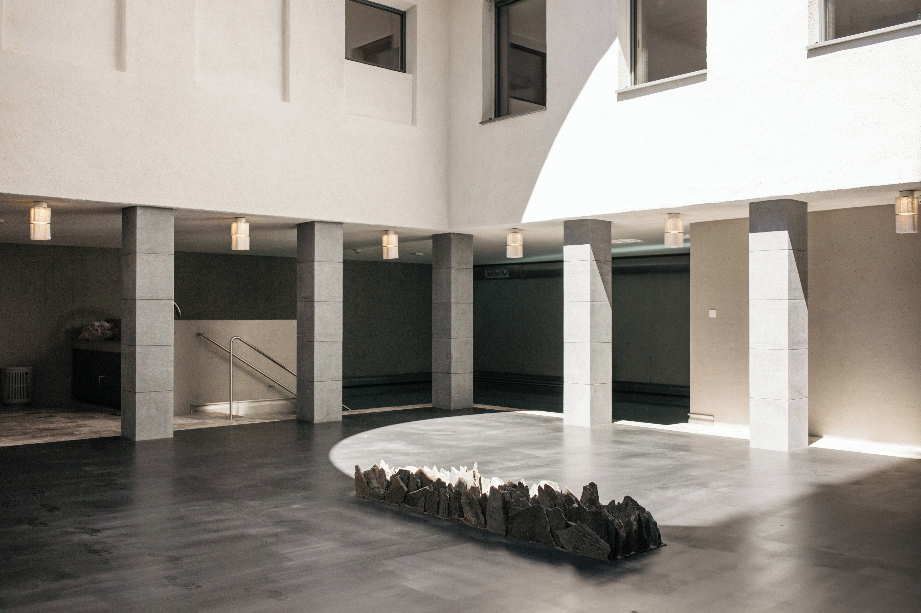 A spacious interior with a central stone feature, large pillars, and a staircase.