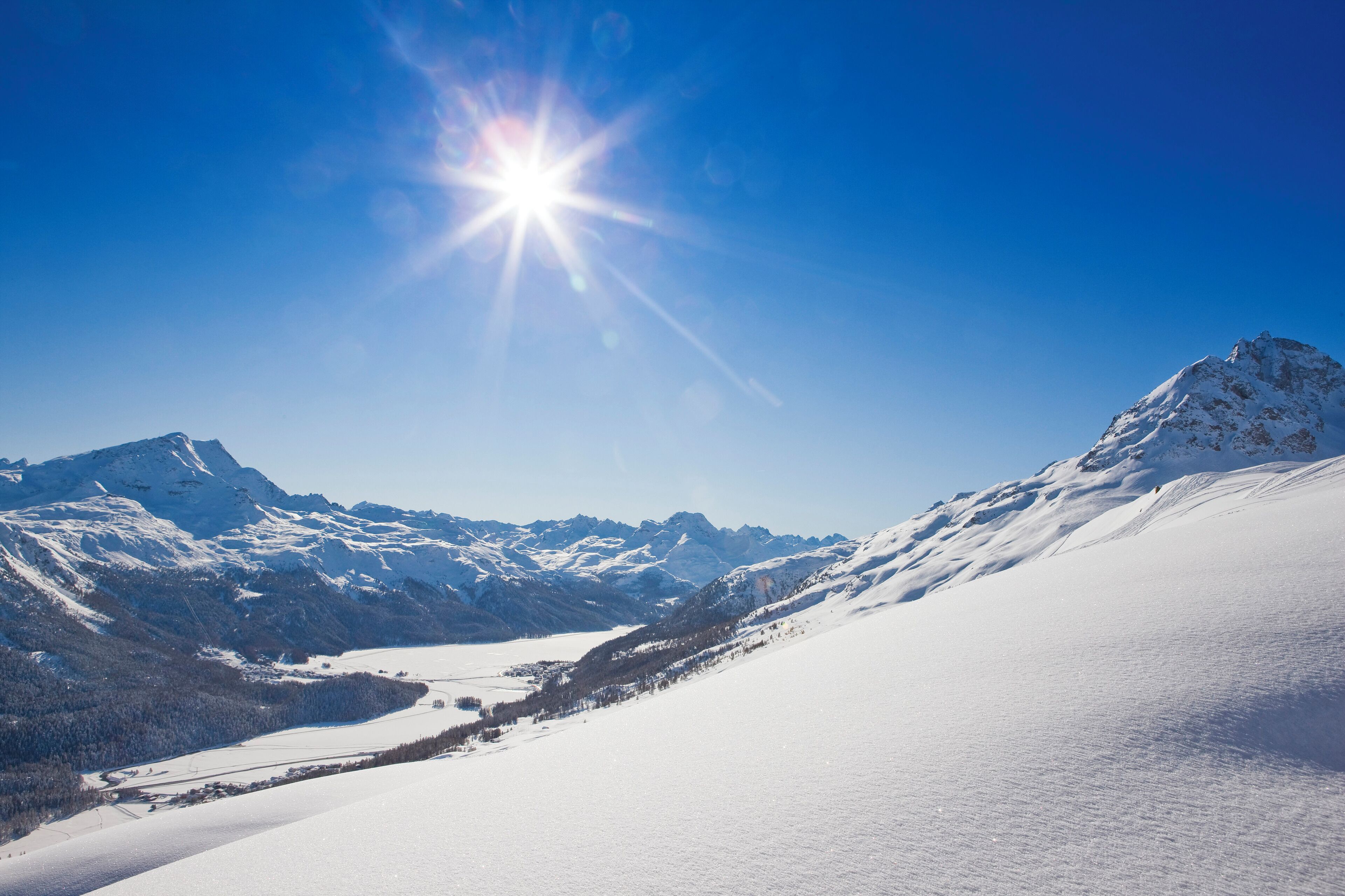 A snow-covered mountain landscape with a clear sky and a bright sun.