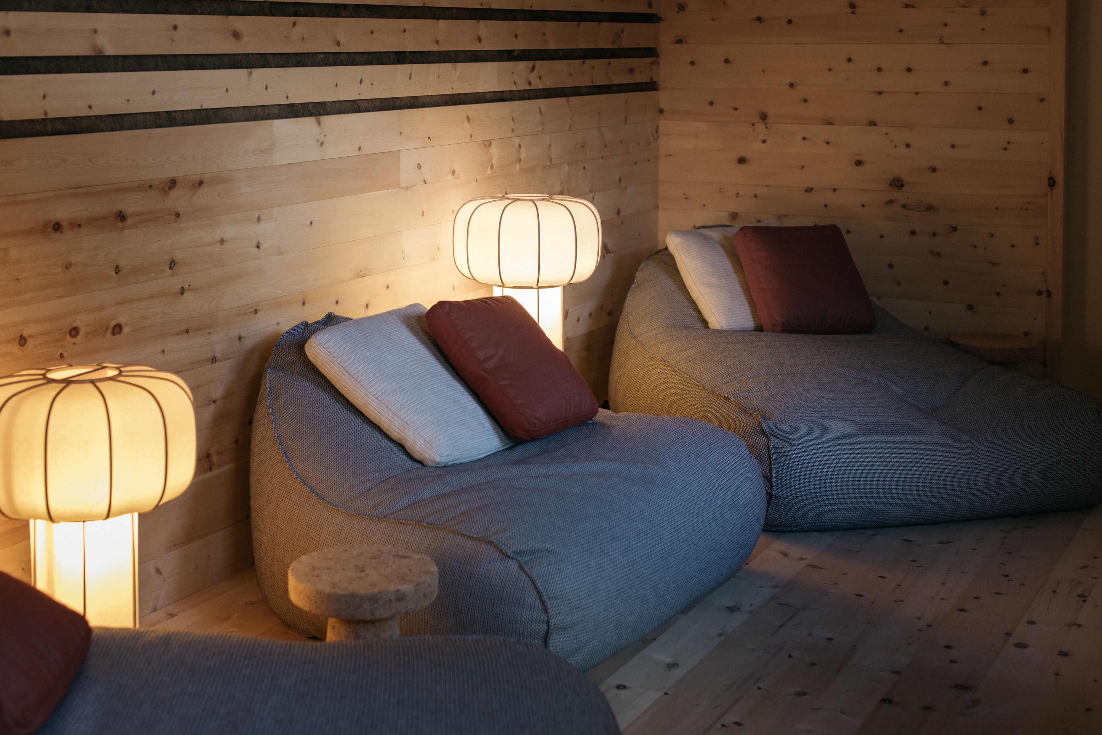 Una habitación acogedora con dos sillones de mimbre, cada uno con un cojín y una pequeña mesa. Dos lámparas de pared proporcionan iluminación.