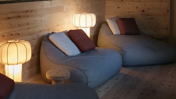 Una habitación acogedora con dos sillones de mimbre, cada uno con un cojín y una pequeña mesa. Dos lámparas de pared proporcionan iluminación.