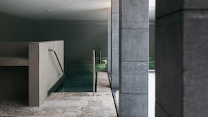 Ein moderner Innenbereich mit Pool, gekennzeichnet durch eine große Glaswand, Steinböden und eine Metallhandrail.