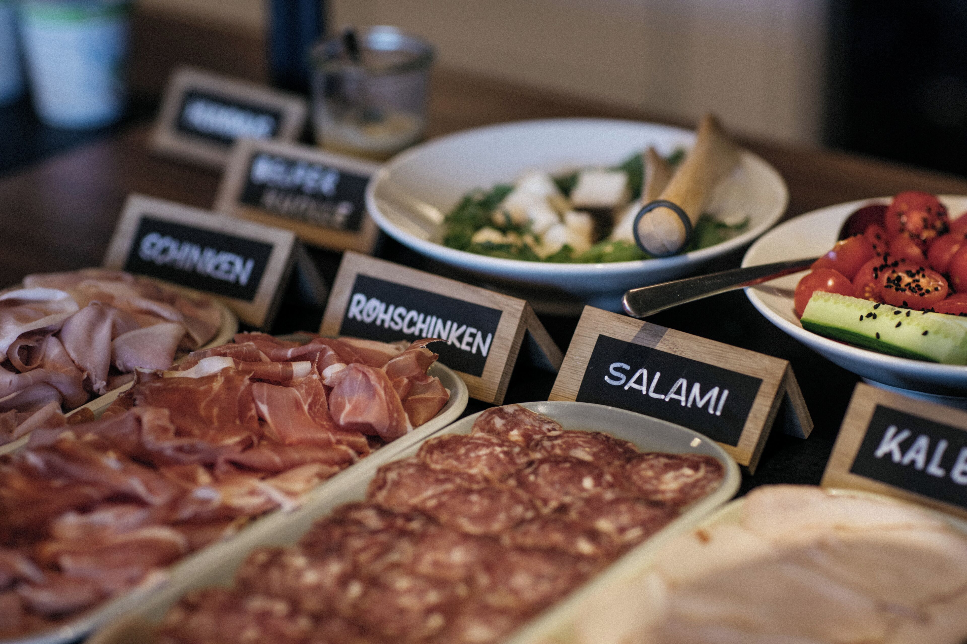 A variety of food items labeled with their names, including salami, and a bowl of salad.